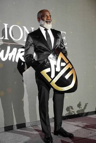 Myron Golden holding an award, dressed in a sharp black suit
